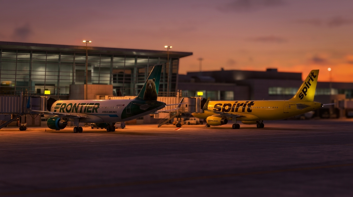 Frontier Airlines green tail Airbus A320 next to Spirit Airlines yellow Airbus A320 parked at adjacent airport gates